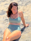 Green swimsuit with hidden-support top and mid-rise bottom, worn while sitting on a sandy beach; relaxed, supportive style.
