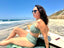 Green swimsuit with hidden-support top and mid-rise bottom, worn while sitting on a sandy beach; calm and comfortable swimwear look.