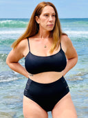 Black swimsuit set with hidden-support top and mid-rise bottom, worn on a sandy beach; sleek, supportive swimwear look.