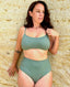 Person wearing green bikini top and bottom, standing against a textured stone wall; vibrant swimwear style.