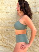 Side view of green bikini top and bottom worn by a person standing against a stone wall; detailed, vibrant swimwear style.