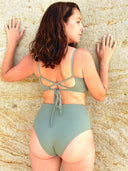 Green swimsuit bottom with crisscross tie-back detail, worn by a person standing with hands resting on a wall.