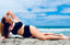 Woman laying on beach with black bikini, showcasing Vie Swimwear.