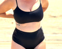 Close-up of black high-waist, mid-thigh swimsuit bottom on a woman; sleek design offers coverage and a flattering silhouette.