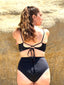 Back view of black swimsuit with hidden-support top and tie-back detail, mid-rise bottom, worn while standing on a rock wall.
