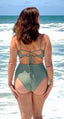 Person wearing green swimsuit with crisscross tie-back top and mid-rise bottom, standing in ocean water; stylish swimwear look.