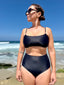 Black swimsuit with hidden-support top and mid-rise bottom, worn on a sandy beach; clean, supportive swimwear look.