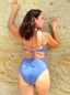 Blue swimsuit bottom with crisscross tie-back detail, worn by a person standing with hands resting on a wall.