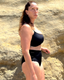 Black bikini top worn near a sandy beach; minimal swimwear style with a relaxed, coastal backdrop.