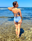 Person wearing blue swimsuit with crisscross tie-back top and mid-rise bottom, standing in ocean water; stylish swimwear look.